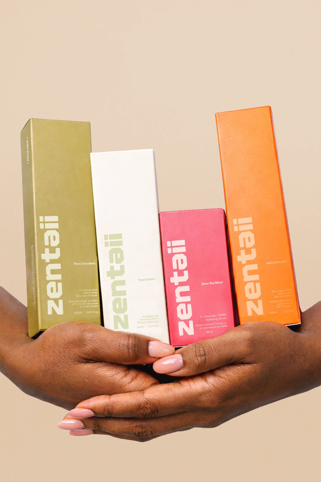 Two hands holding four Zentaii cartons fanned out — olive, cream, pink and orange, each with the wordmark set vertically.