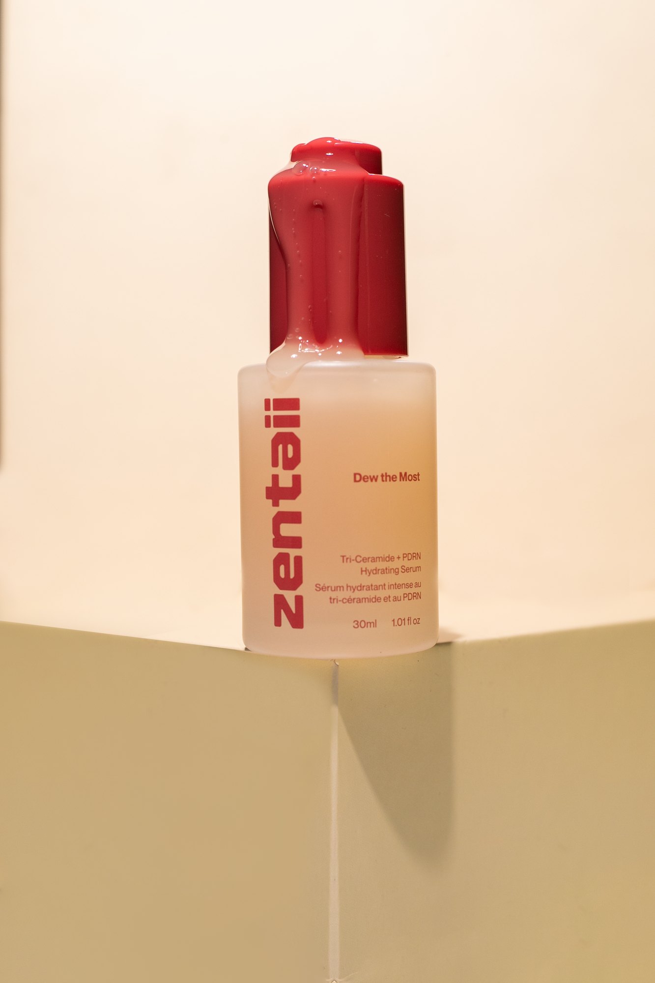 The serum bottle on a low plinth in raking light, shadow running across the cream set.