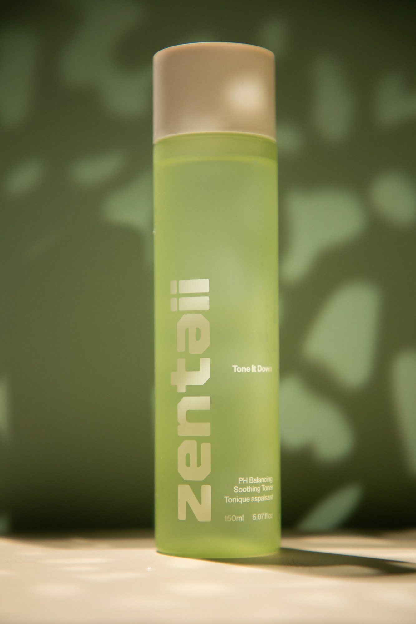 The green toner bottle in dappled foliage light against a deep green wall.